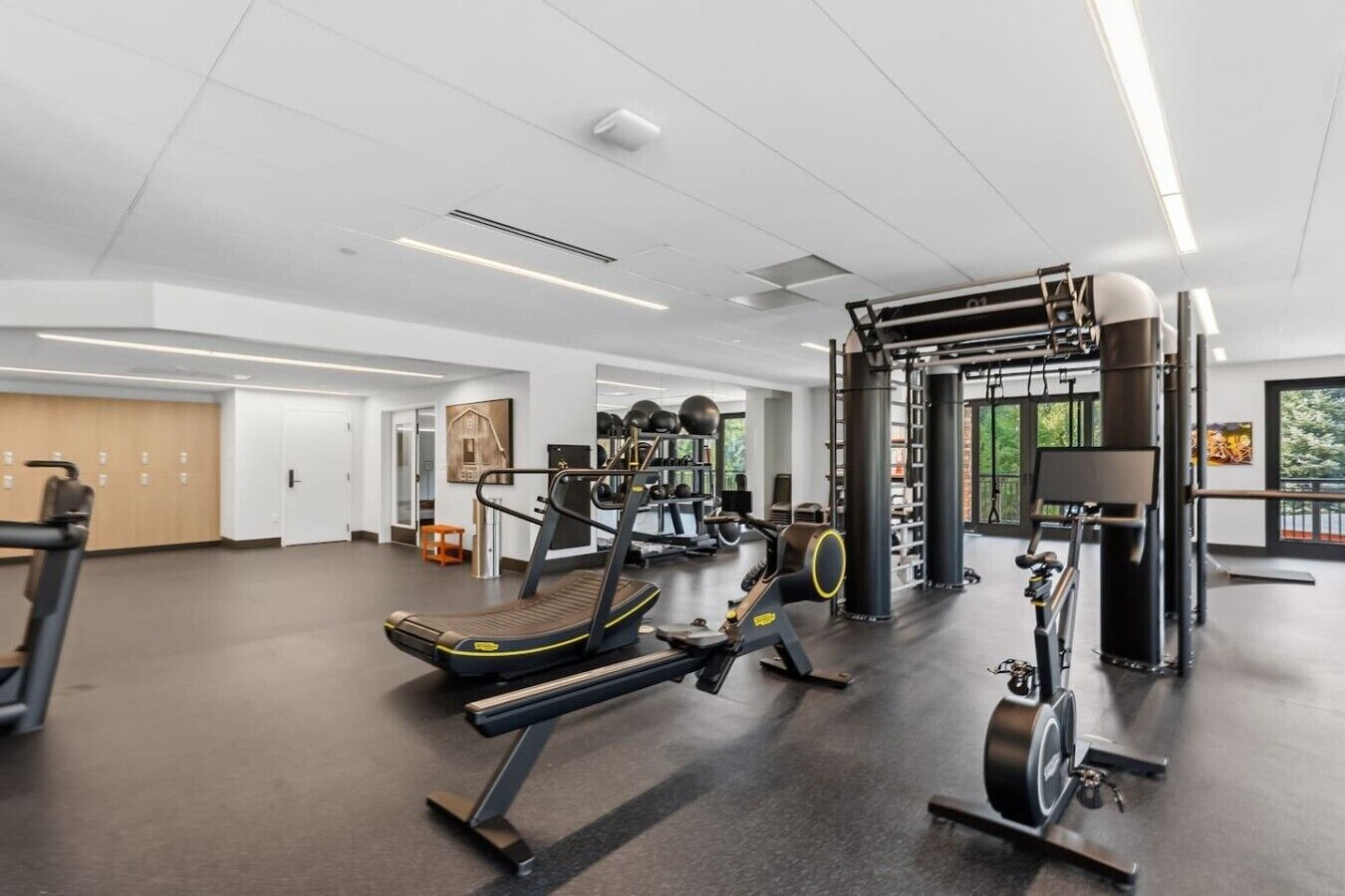A modern gym with various exercise equipment, including treadmills and weight machines, and a large window providing natural light.