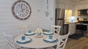 A dining area with a round table, white chairs, and a wall-mounted clock. - First Floor • Closest to Private Beach • Newly Renovated • Pools & Amenities (Hilton Head Island)