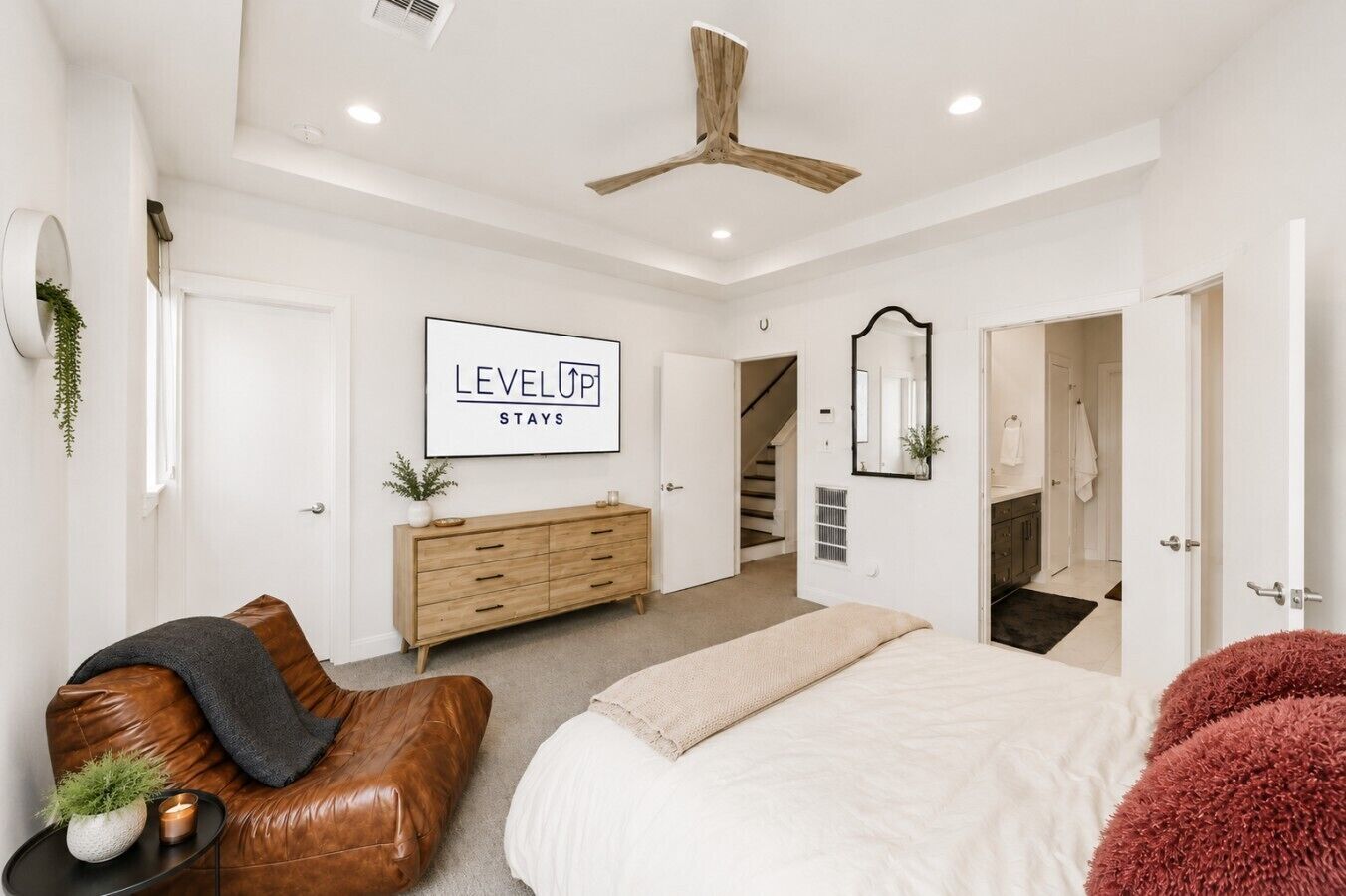 A modern bedroom with a bed, a wooden dresser, a brown leather sofa, a ceiling fan, and a staircase leading to another room.