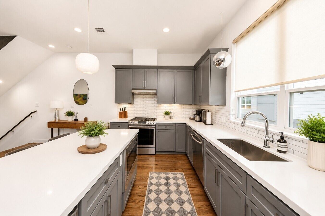 A modern kitchen with grey cabinets, a white countertop, and a stainless steel sink.
