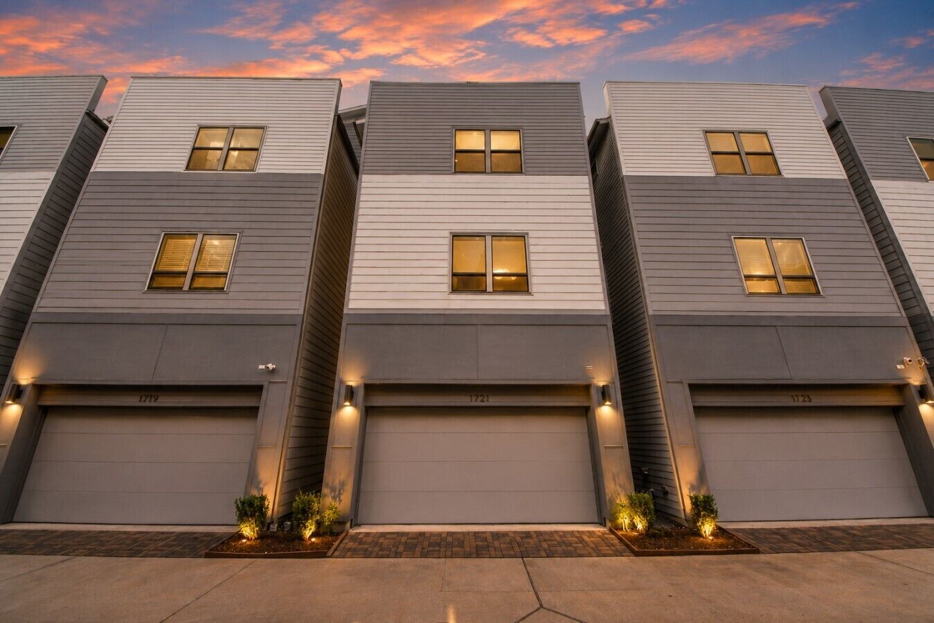 A row of modern residential buildings with uniform design, featuring garage doors and small landscaped areas at the base.