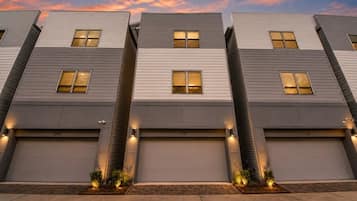 A row of modern residential buildings with uniform design, featuring garage doors and small landscaped areas at the base.