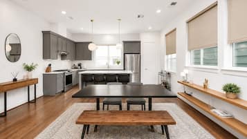A modern kitchen with a central island, dark wooden dining table, and pendant lighting.