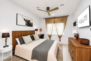 A modern bedroom with a bed, bedside tables, a ceiling fan, and a window with curtains.
