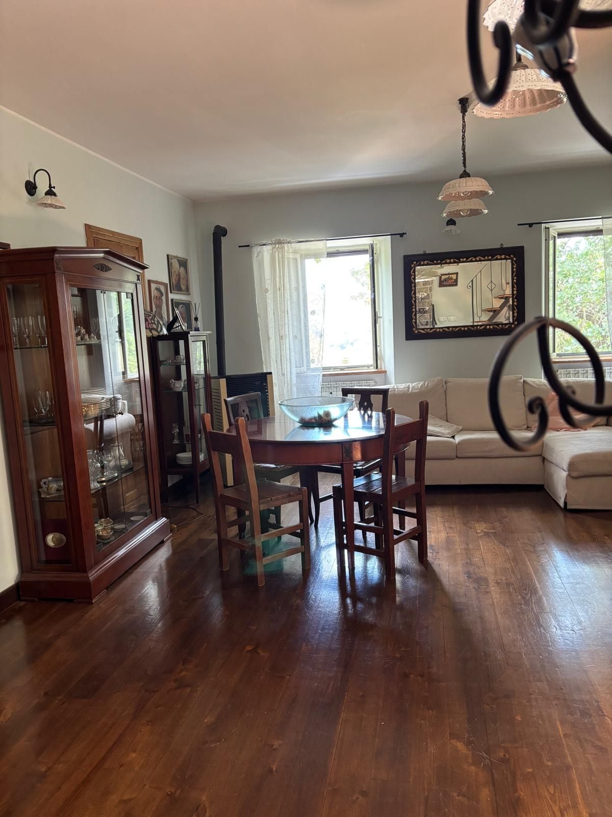 Un comedor con una mesa y sillas de madera, un armario con puertas de cristal, un sofá y una ventana con cortinas.