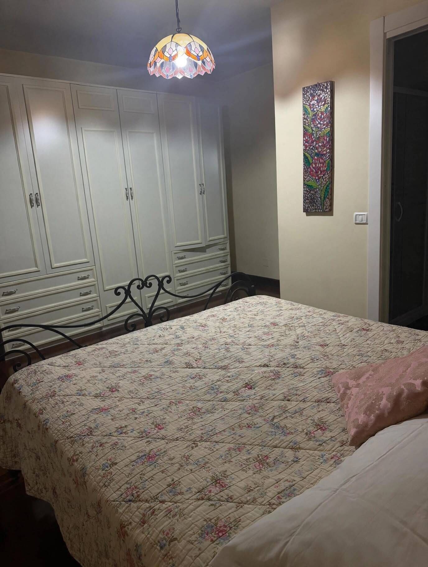 Ein Schlafzimmer mit einem Bett, einem Kleiderschrank, einer Pendelleuchte und einem Wandbild.