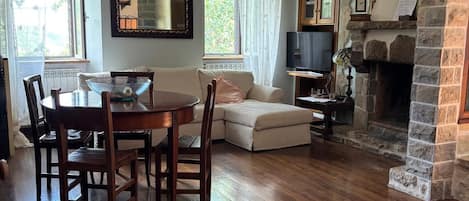 A living room with a fireplace, a dining table with chairs, a sofa, and a television.