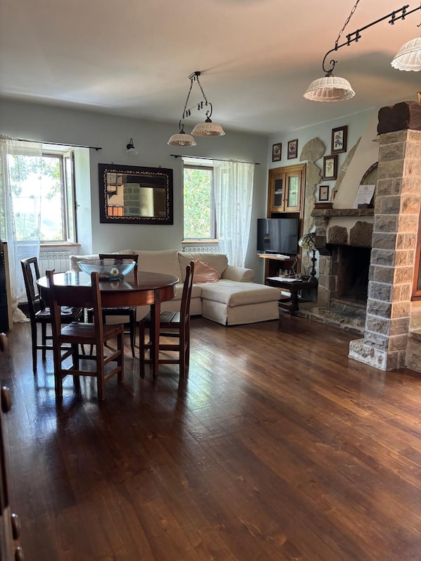 A living room with a fireplace, a dining table with chairs, a sofa, and a television.