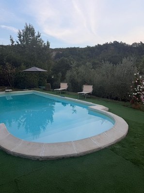 A swimming pool with a surrounding grassy area and a few lounge chairs.