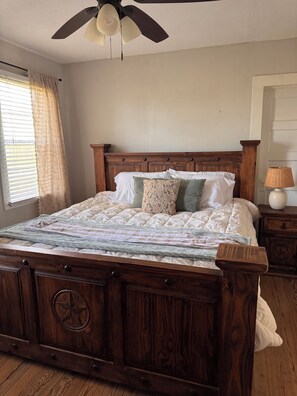 A bedroom with a wooden bed, a ceiling fan, a window with curtains, and a bedside table with a lamp. - Charming 3-bedroom farmhouse in Damon (Damon)
