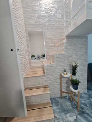 A staircase with a white brick wall and a wooden floor leading to a landing with potted plants. - Furnished and fully equipped Piazza Plebiscito House on Via Toledo in downtown Naples (Napoli)
