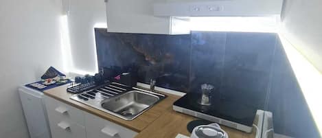 A compact kitchen with a sink, stove, and a coffee maker on a small table.