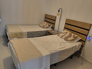 Quarto com duas camas, cada uma com cabeceira de madeira, mesa de cabeceira e luminária.