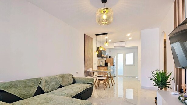 Ein modernes Wohnzimmer mit einer Couch, einem Essbereich mit Tisch und Stühlen sowie einer Küche im Hintergrund.