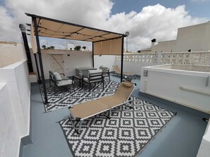 A rooftop terrace with a patterned floor, a sun lounger, a table with chairs, and a covered seating area. - Tranquil oasis in Costa Blanca (VC)