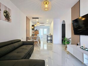 A modern living room with a sectional sofa, a dining area with a table and chairs, a kitchen in the background, and a flat-screen TV mounted on the wall. - Tranquil oasis in Costa Blanca (VC)