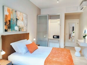 Een moderne slaapkamer met een bed, nachtkastje, bedlamp, kledingkast, spiegel en een zichtbare badkamer door een open deur.