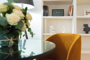 A room with a glass table, a yellow chair, a white bookshelf, and a vase with white flowers. - 3-Bedroom, 3-Bathroom Premium Vatican Apartment - Free Luggage Storage Included (Roma)