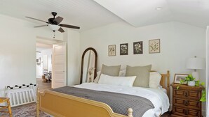 Ein Schlafzimmer mit einem Bett, einem Schminktisch, einem Spiegel und einem Deckenventilator.