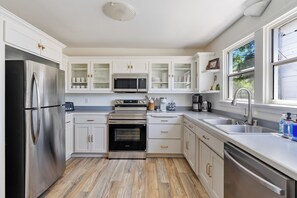 A modern kitchen with white cabinetry, stainless steel appliances, and a wooden floor.