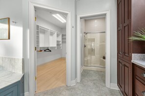 Ein modernes Badezimmer mit bodenebenen Dusche, einem Waschtisch mit Marmorplatte und einem begehbaren Kleiderschrank mit offenen Regalen.