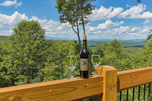 A bottle of wine on a wooden deck with a scenic view of trees and mountains in the background. - Painted Sky Lodge| Blue Ridge, GA (Morganton)