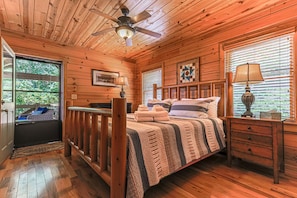 A wooden cabin bedroom with a bed, a nightstand, a ceiling fan, and a window with blinds. - Painted Sky Lodge| Blue Ridge, GA (Morganton)