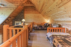 A cozy cabin interior with a loft bed, a dining area, and a stone wall. - Painted Sky Lodge| Blue Ridge, GA (Morganton)