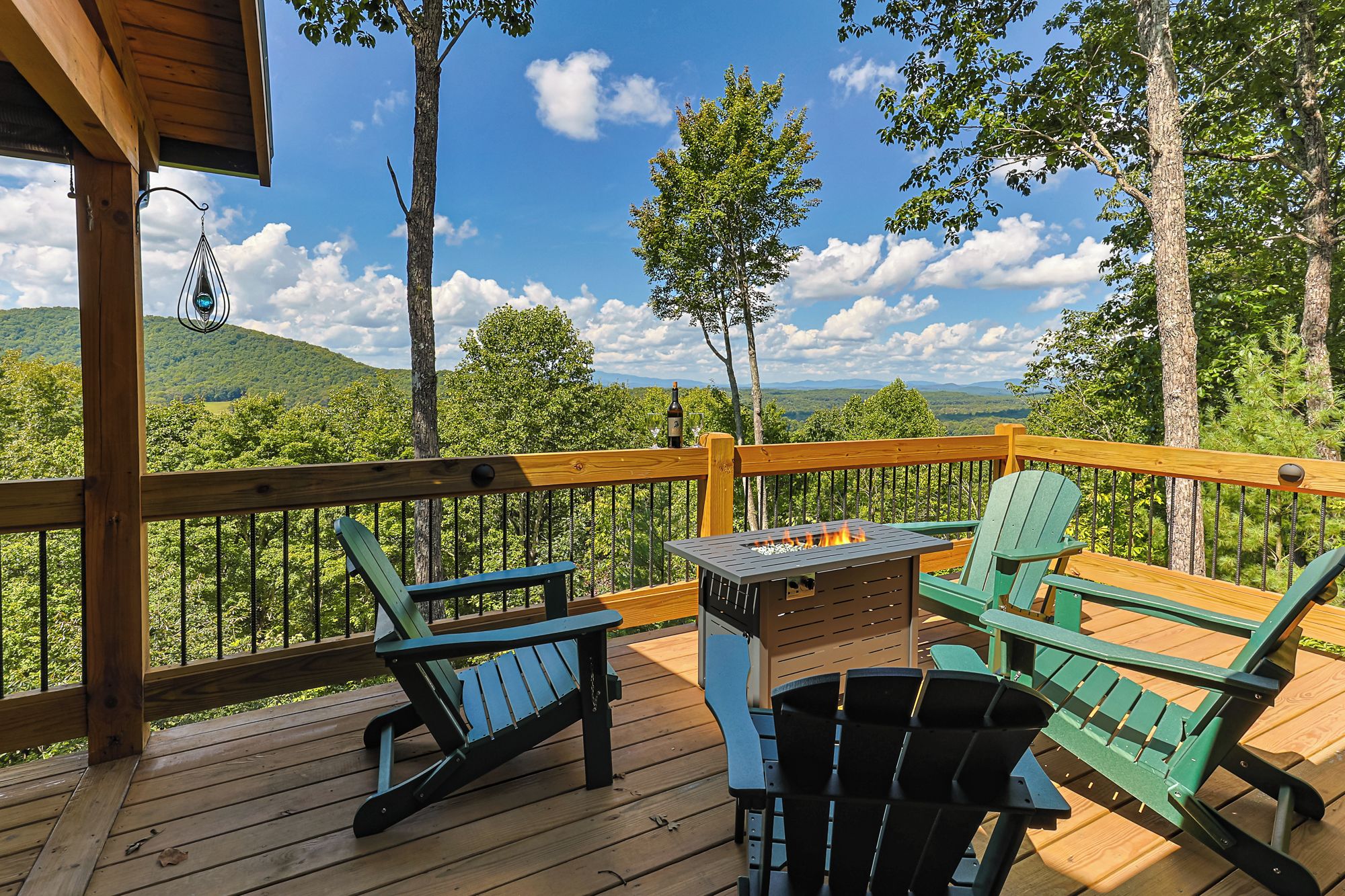 A deck with Adirondack chairs, a table with a grill, and a view of a forested landscape.