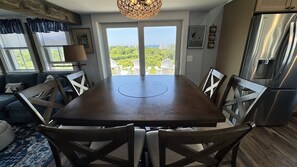 A dining area with a wooden table and chairs, a view of the outdoors, and a modern kitchen with a stainless steel refrigerator. - 4 BR/2 BA Charmer! Sunset and Ocean Views, Steps to the Beach! (New Shoreham)