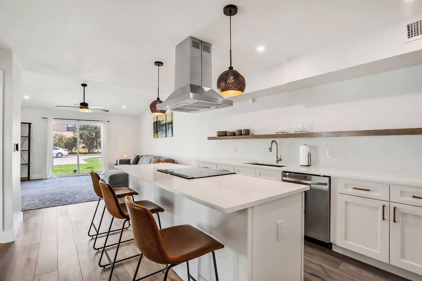 A modern kitchen with a central island, bar stools, pendant lighting, and a view of the outdoors.