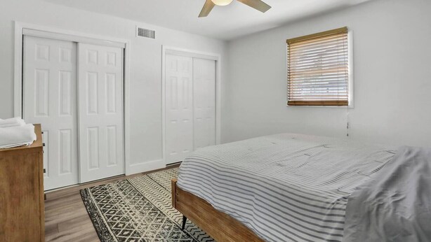A bedroom with a bed, a ceiling fan, a window with blinds, and a patterned rug. - 3BR/2B Retreat - Walk to town (St. Augustine)