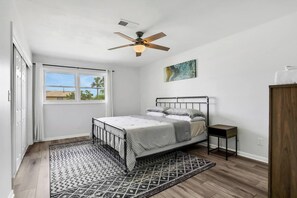 A bedroom with a bed, a ceiling fan, a window with a view, a painting, and a wooden cabinet. - Spacious 3BR/2BA Retreat - Walk to town (St. Augustine)
