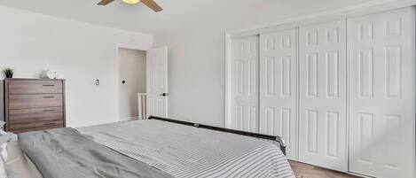 Une chambre à coucher avec un lit, une commode en bois, un ventilateur de plafond et une porte double blanche.