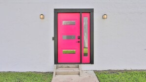 A bright pink door with a black frame, set in a white wall with two wall-mounted lights. - 3BR/2B Retreat - Walk to town (St. Augustine)
