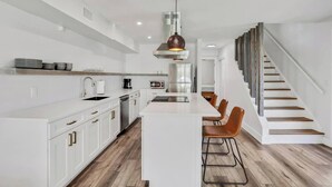 A modern kitchen with white cabinetry, a central island, and a dining area with bar stools. - 3BR/2B Retreat - Walk to town (St. Augustine)