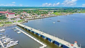 A coastal cityscape with a prominent bridge, marina, and a large building with a red roof. - 3BR/2B Retreat - Walk to town (St. Augustine)