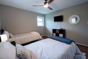 Un dormitorio con dos camas, ventilador de techo, televisión, ventana y cómoda.