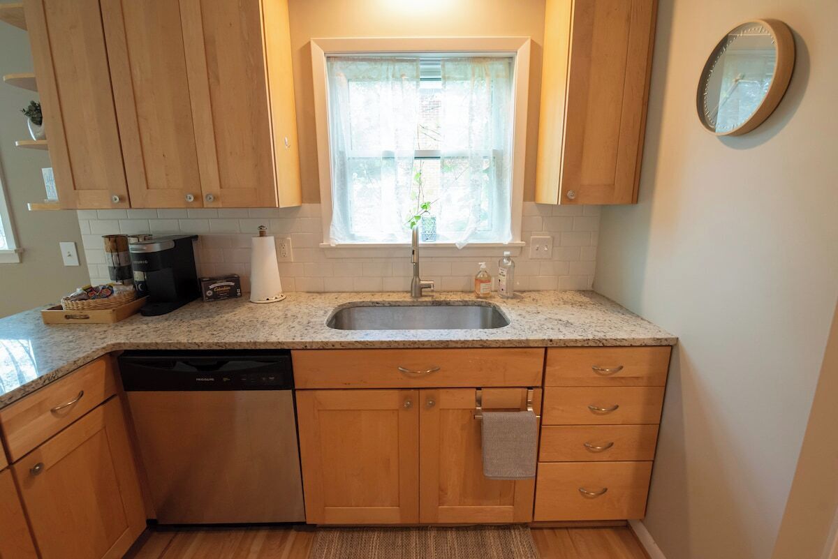Una cocina con armarios de madera, encimera de granito, pileta de acero inoxidable y una ventana con planta.
