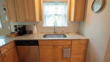 Una cocina con armarios de madera, encimera de granito, pileta de acero inoxidable y una ventana con planta.