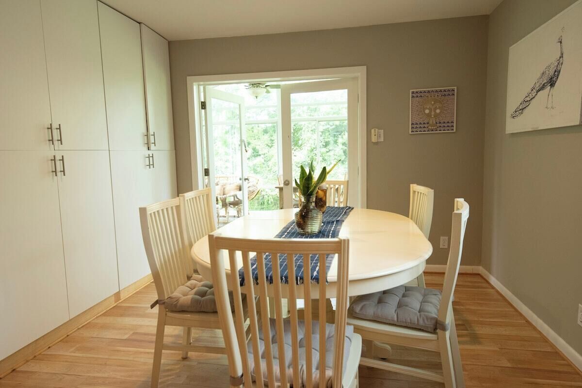 A dining area with a round table, white chairs, and a view through a glass door.