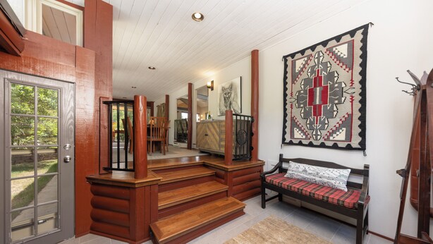 Una escalera de madera que sube a un rellano del segundo piso, con un banco y una alfombra.