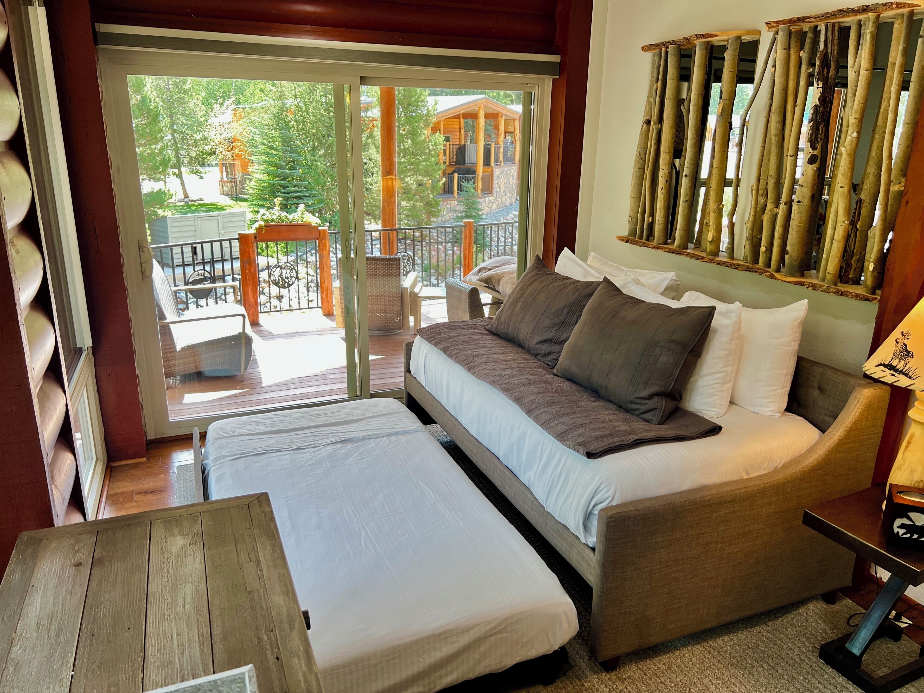 A room with a sofa bed, a small table, and a view of an outdoor deck with a railing.