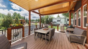 Una terraza techada con mobiliario exterior, una parrilla y vistas a un lago y bosque.