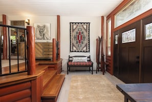 A wooden staircase leading to a bench with a patterned rug, a wall-mounted tapestry, and a door with stained glass windows.