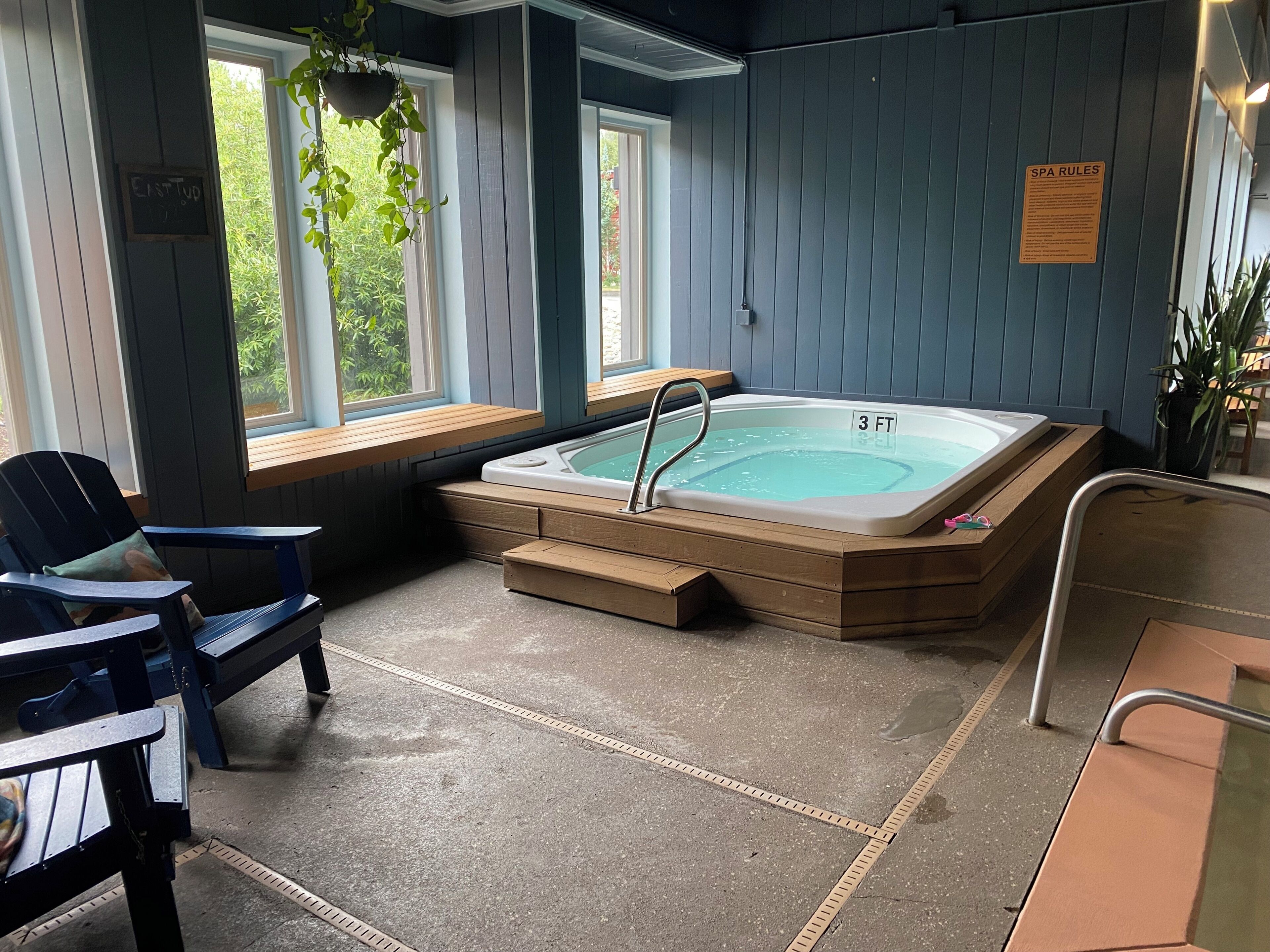 Área de spa com hidromassagem, bancos de madeira e uma placa com as regras do spa.