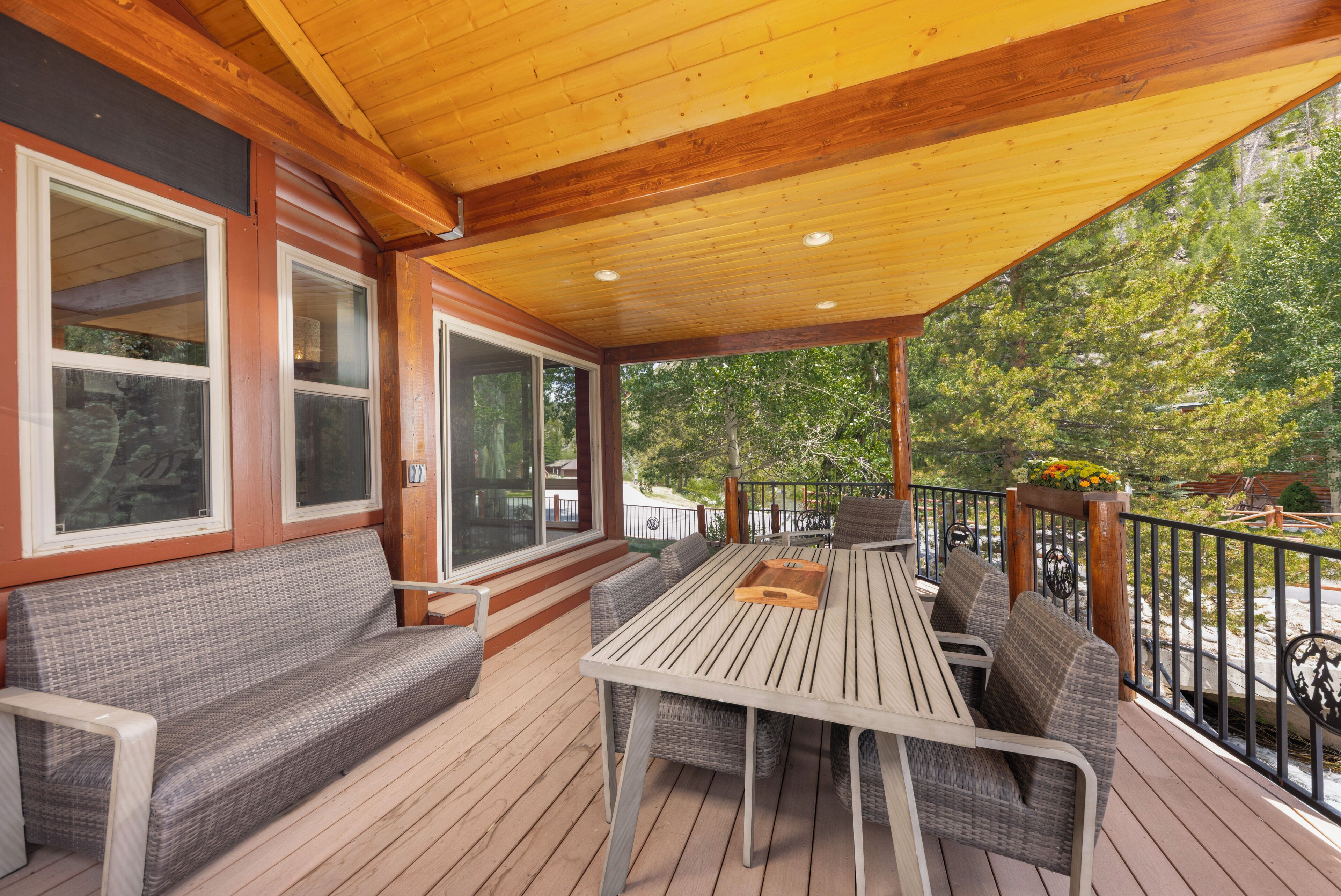 An outdoor deck with a wooden table and chairs, a cushioned bench, and a railing.