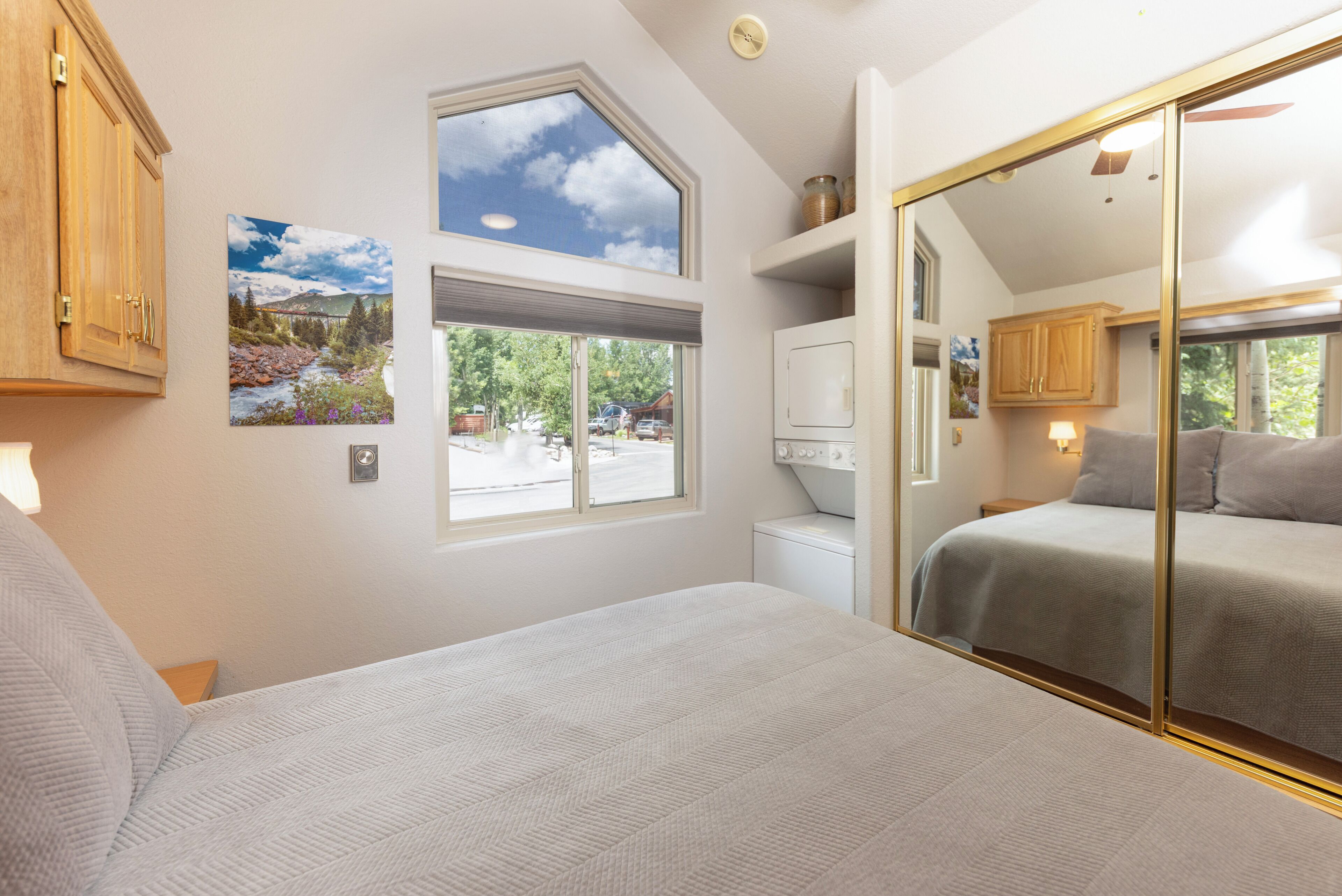 A bedroom with a large bed, a window with a view of a parking lot, and a washing machine.