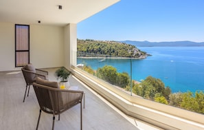 Ein Balkon mit Blick auf eine Küstenlandschaft, ein Tisch mit einer Pflanze und zwei Stühle.