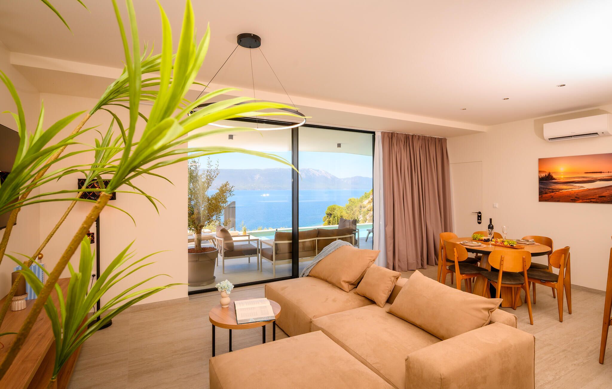 A modern living room with a sofa, dining table, chairs, and a large window with a view of the sea.